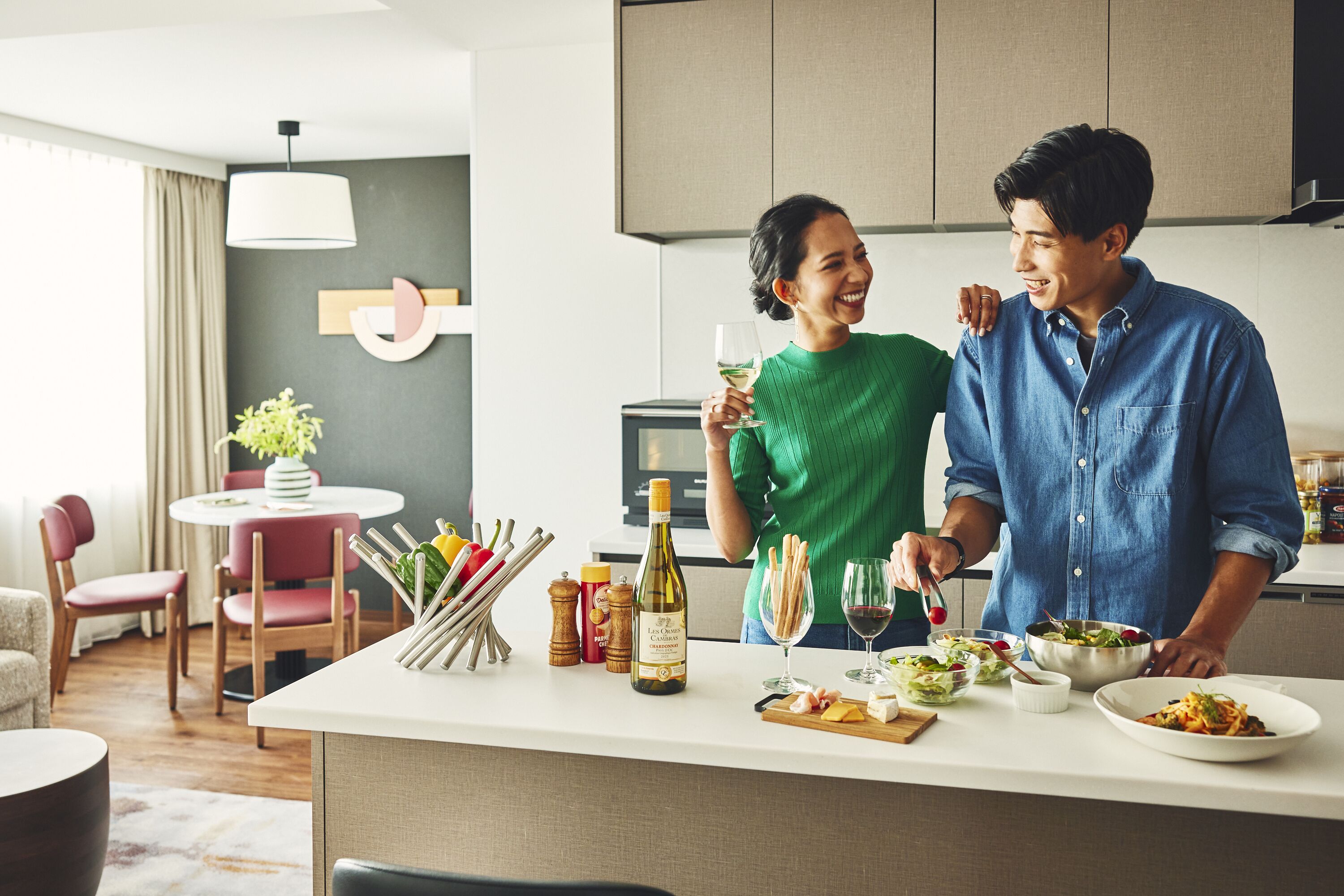A modern kitchen with a dining area, featuring a central island with food items, a wine bottle, and kitchen utensils.