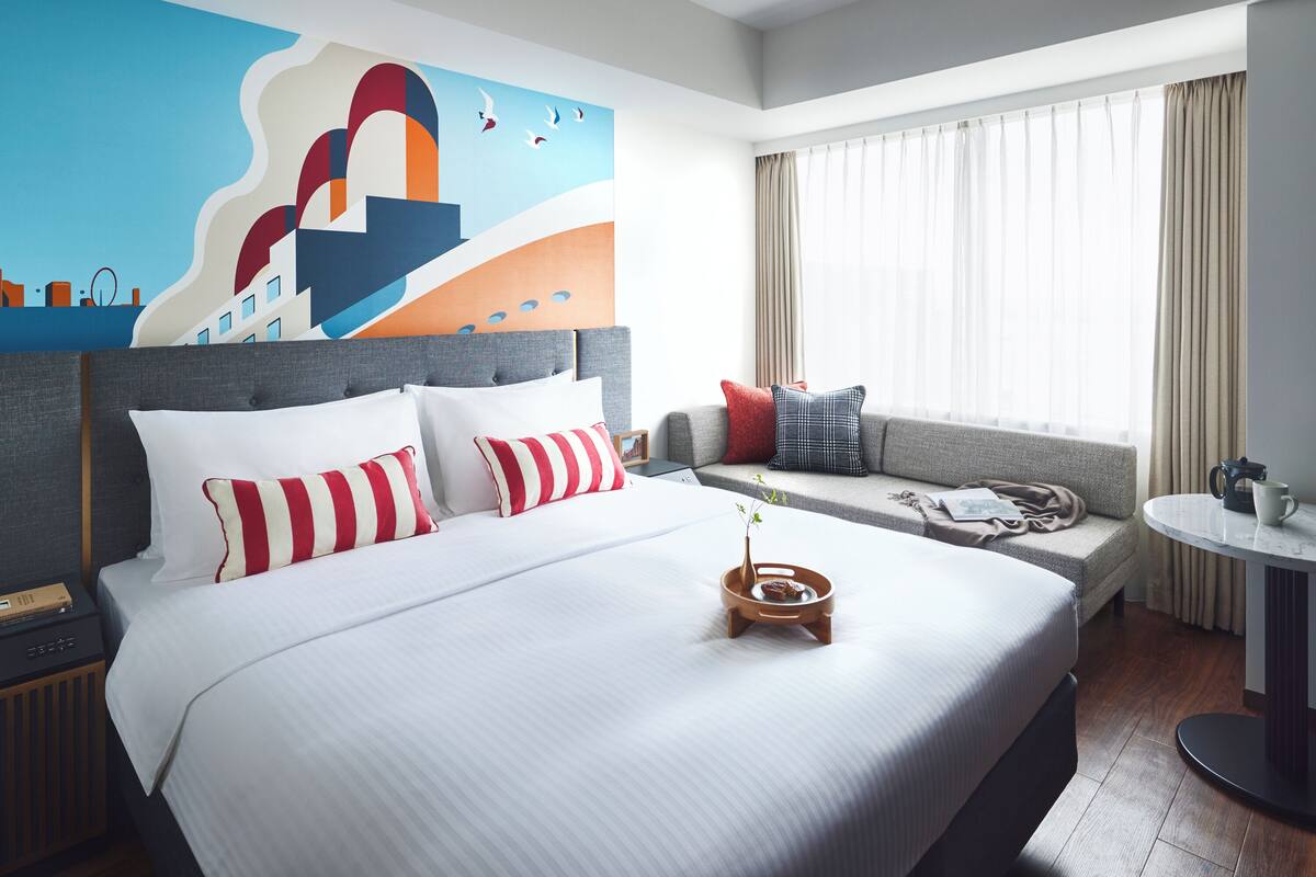 A hotel room with a large bed, a sofa, a small table, and a window with curtains.