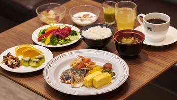 A wooden table with various dishes including fish, vegetables, and rice. There are also bowls of soup and a cup of coffee.