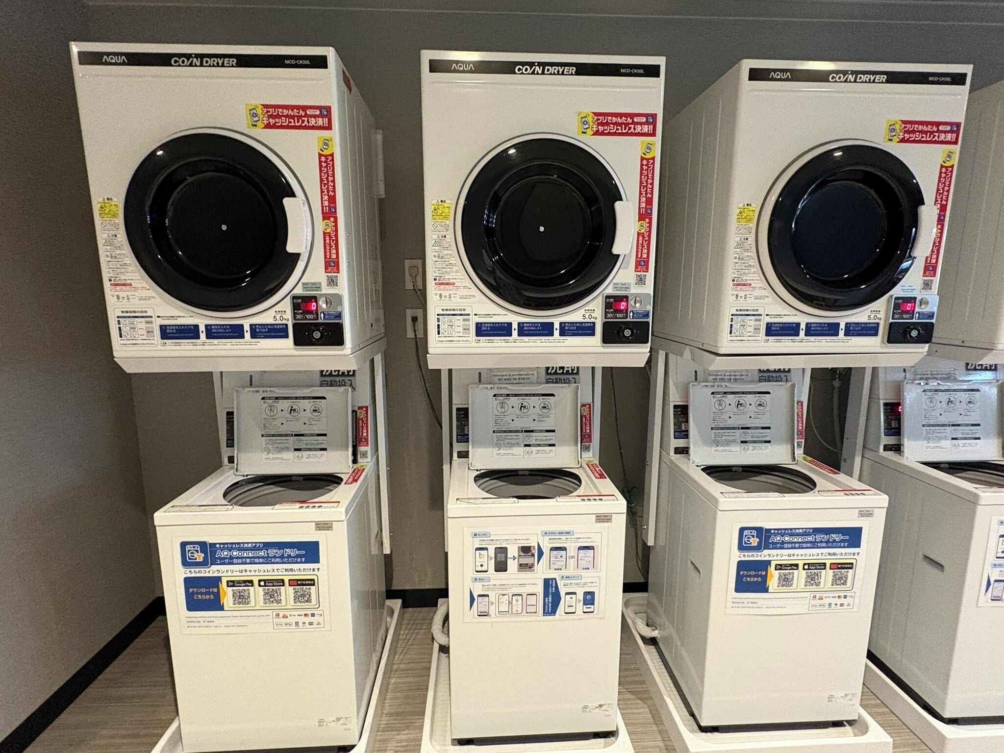 Three stacked laundry machines with control panels and instructions.