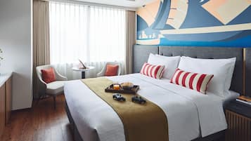 A hotel room with a large bed, a desk, a chair, a window with curtains, and a wall mural.