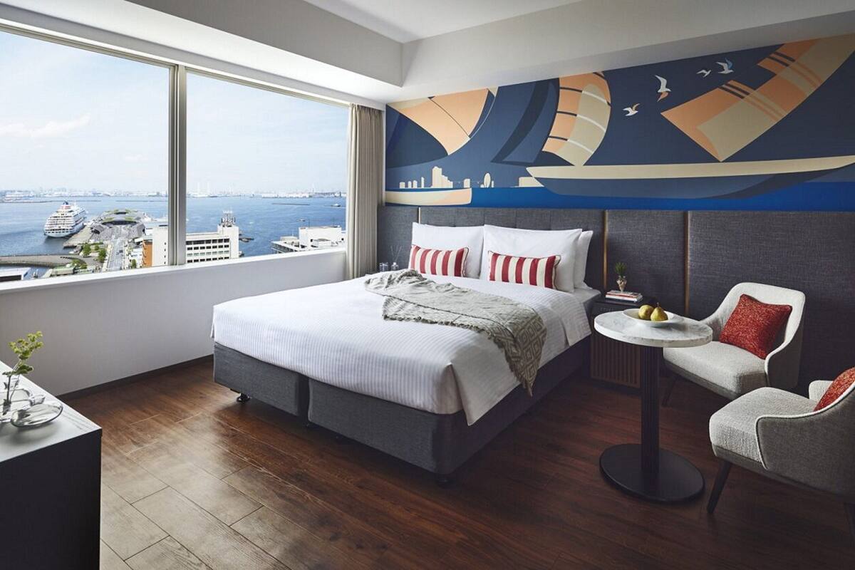 A modern hotel room with a large bed, a small round table, and a view of the city and water.