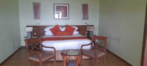 A bedroom with a bed, two chairs, a small table, and a nightstand. - CAPELLA RESORT (Nakuru)