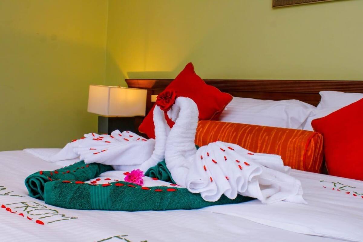 Una cama bien hecha con almohadas blancas y rojas, una toalla verde y un arreglo decorativo de toallas con forma de cisne.