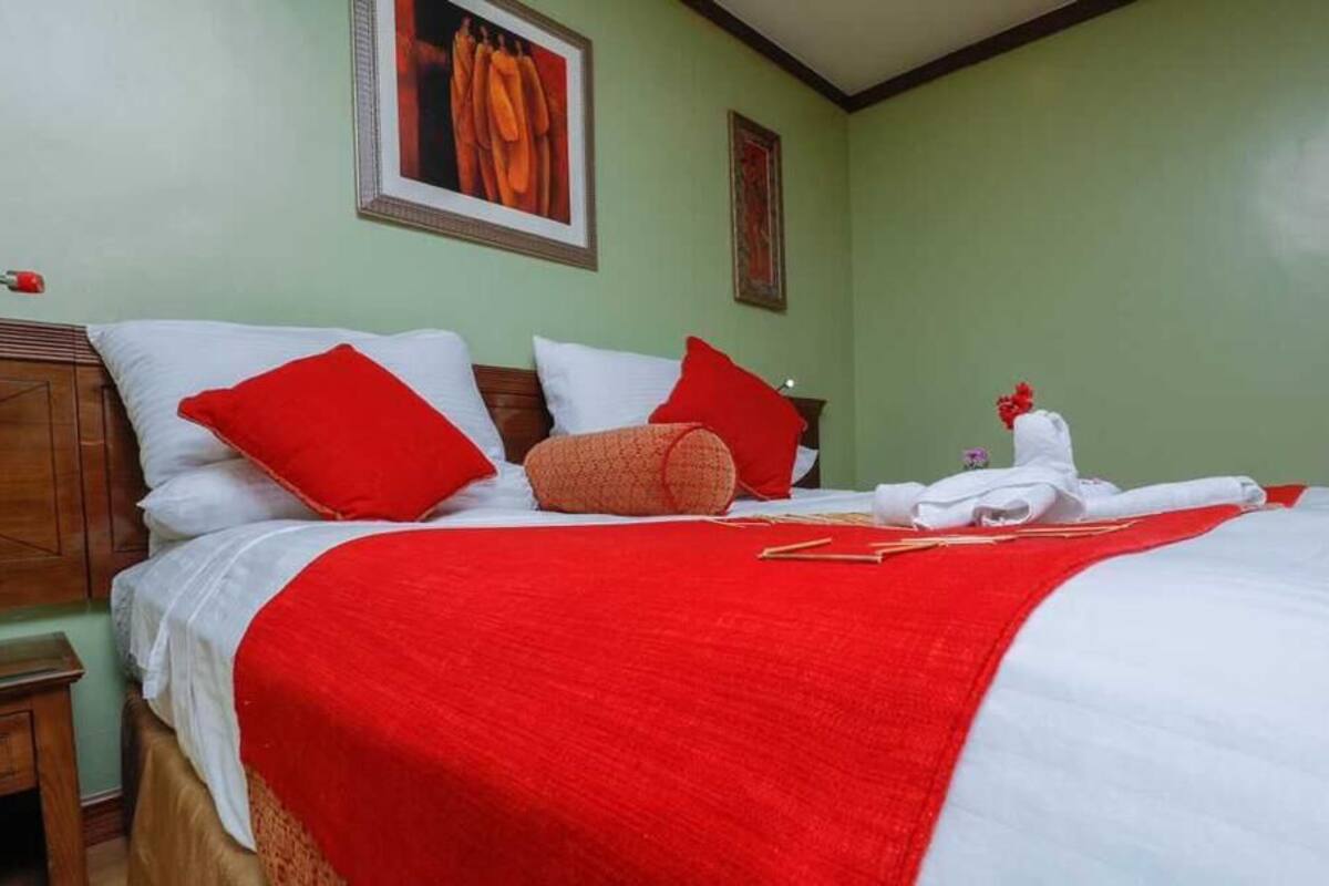 Una cama bien hecha con ropa de cama roja y blanca, un cabecero de madera y una manta roja.
