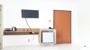 A compact room with a wooden door, a small white refrigerator, a mounted television, and a shelf with a kettle and a mug. - Patong Bay Inn (Patong)