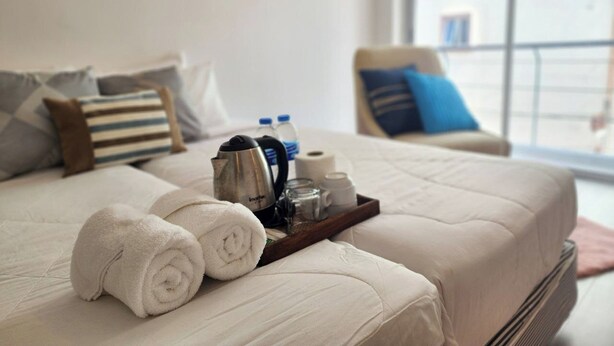 A neatly made bed with rolled white towels, a tray with toiletries, and a window view of buildings. - Patong Bay Inn (Patong)