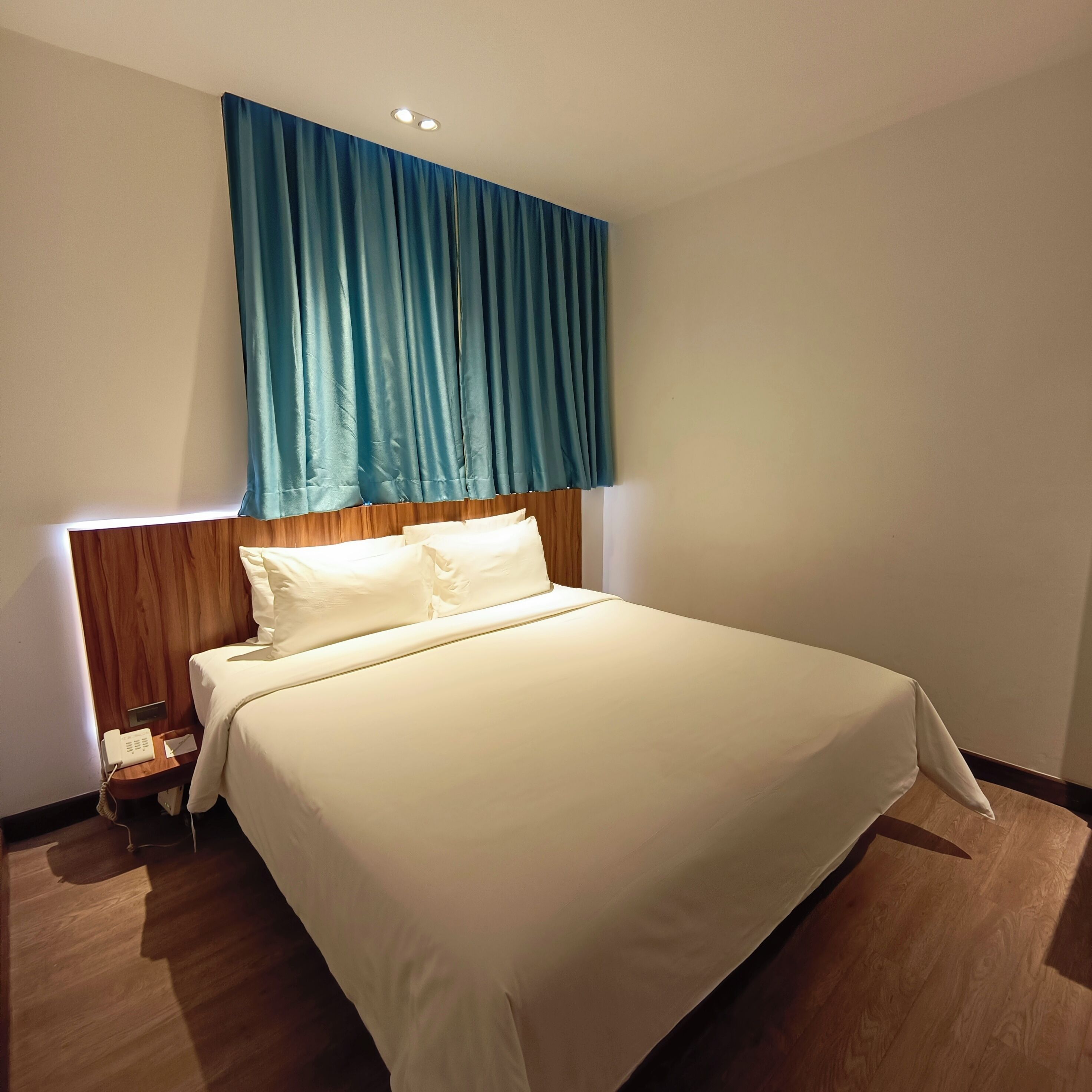 A hotel room with a large bed, wooden headboard, and a blue curtain.