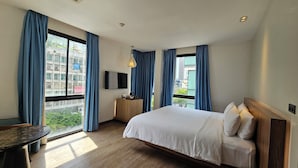 Une chambre d’hôtel avec un lit, un bureau, une télévision et de grandes fenêtres équipées de rideaux.