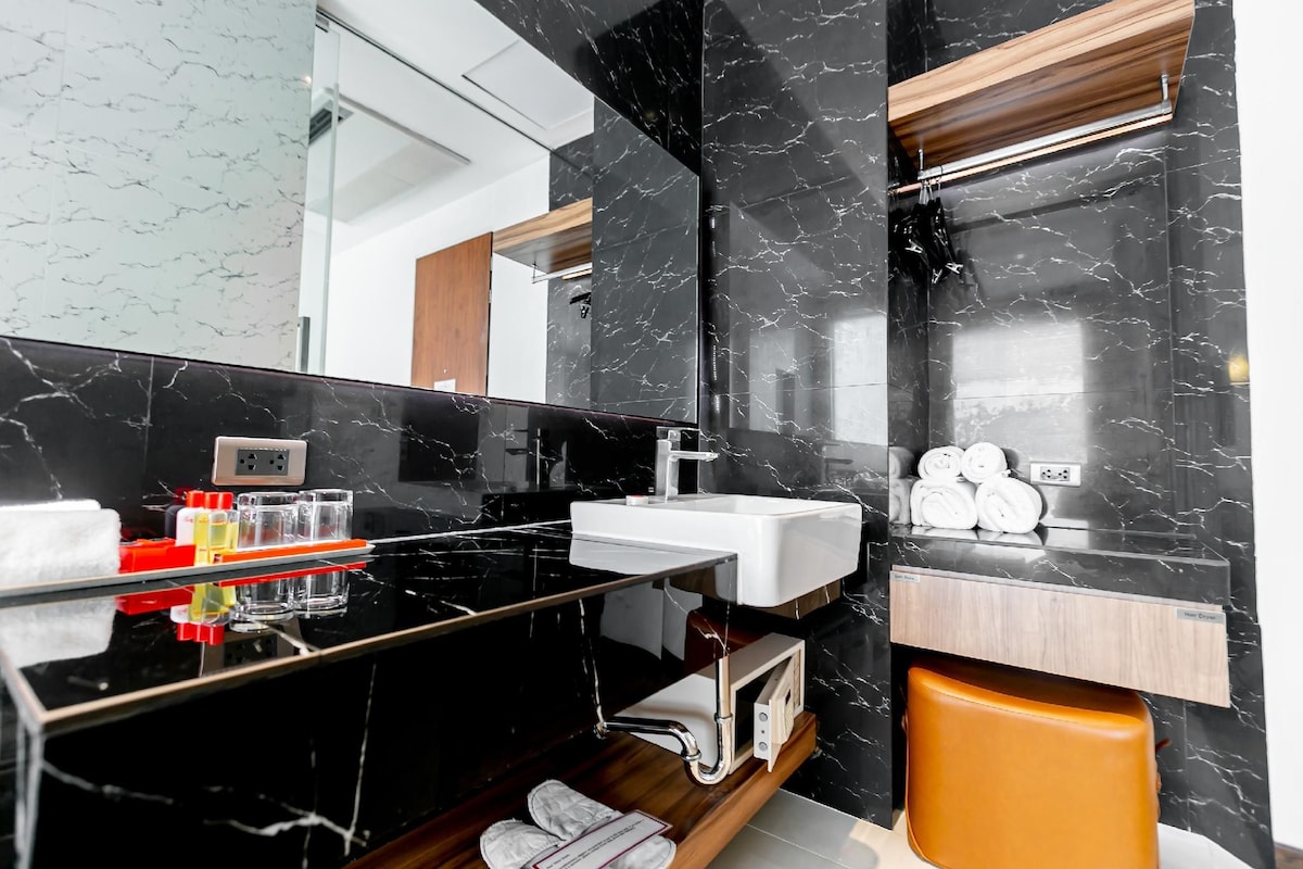 A modern bathroom with a black marble vanity, a white sink, and a wooden shelf above the sink.