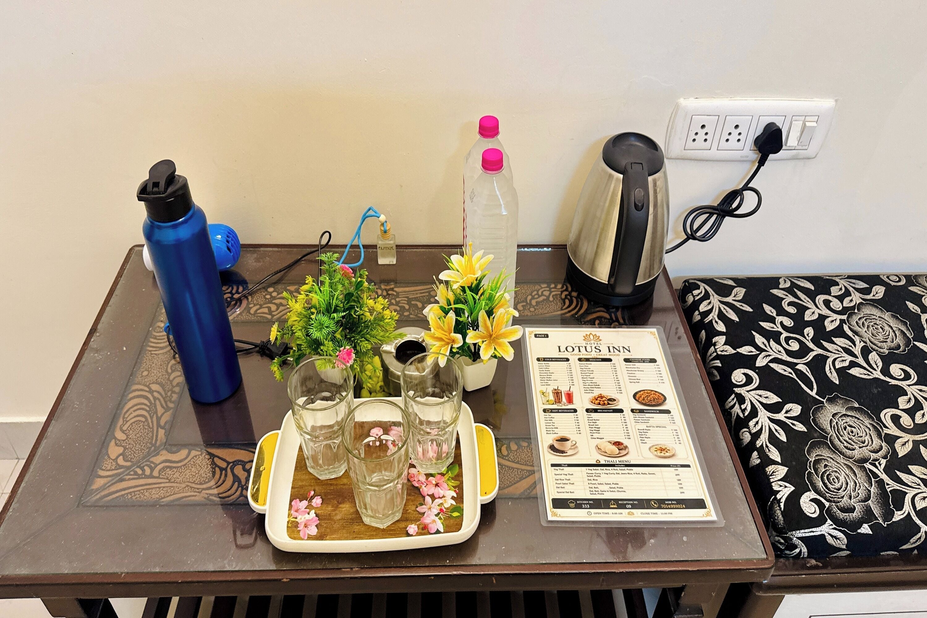 A table with a menu, a water bottle, a kettle, and a small plant.