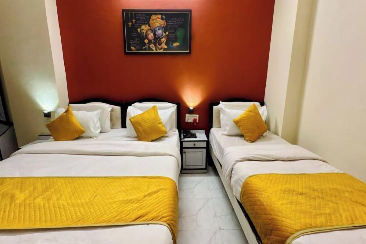Habitación de hotel con dos camas, cada una con ropa de cama blanca y una manta amarilla. Hay una mesita de noche con una lámpara entre las camas, y una obra de arte colgada en la pared sobre el cabecero.