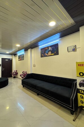 A lobby with a black sofa, a door labeled '104', and a wall-mounted air conditioning unit. - Hotel Lotus Inn (Udaipur)