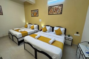 A hotel room with two beds, each with white linens and yellow accents, a nightstand with a lamp, and a small desk with a plant. - Hotel Lotus Inn (Udaipur)