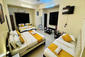 A hotel room with two beds, a desk, a TV, and an air conditioning unit.