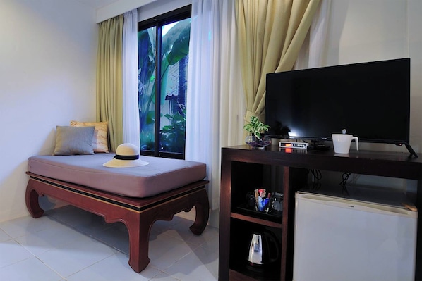 Quarto com cama, televisão, mini-frigorífico e janela com cortinas.