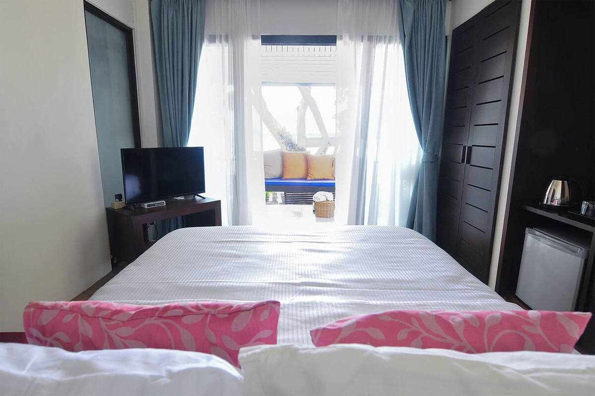 Camera d'hotel con un letto, una TV, una scrivania e vista su un balcone con ringhiera blu.