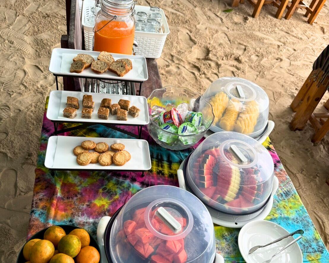 A buffet table with various food items and drinks on a beach setting.