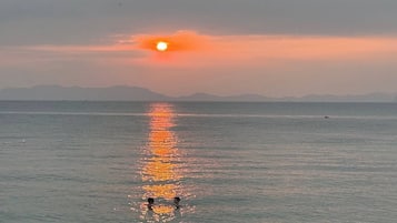 Een zonsondergang boven een rustige zee, met twee mensen die op de voorgrond zwemmen.