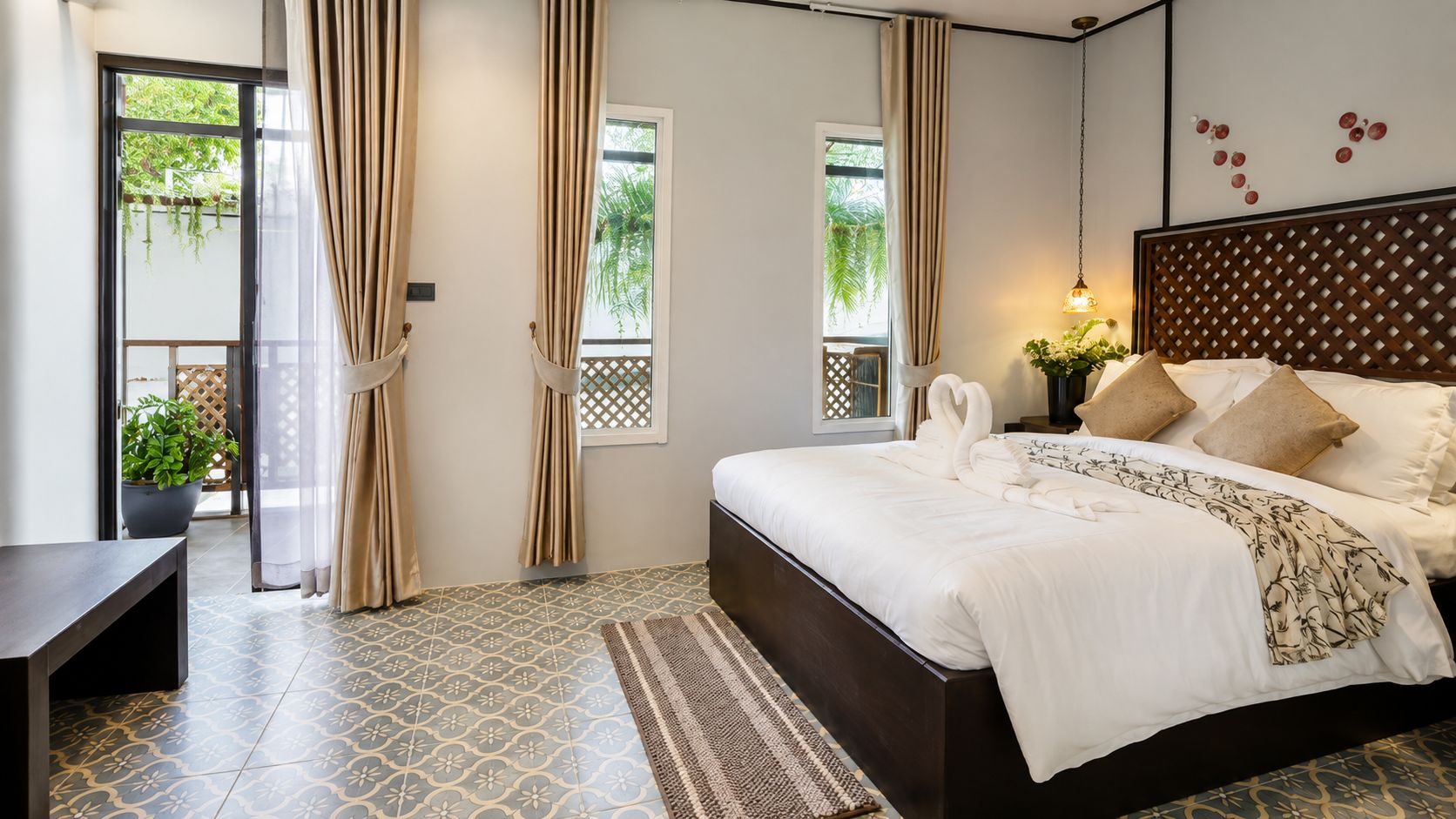 A bedroom with a bed, curtains, a window, a potted plant, and a wall-mounted light fixture.