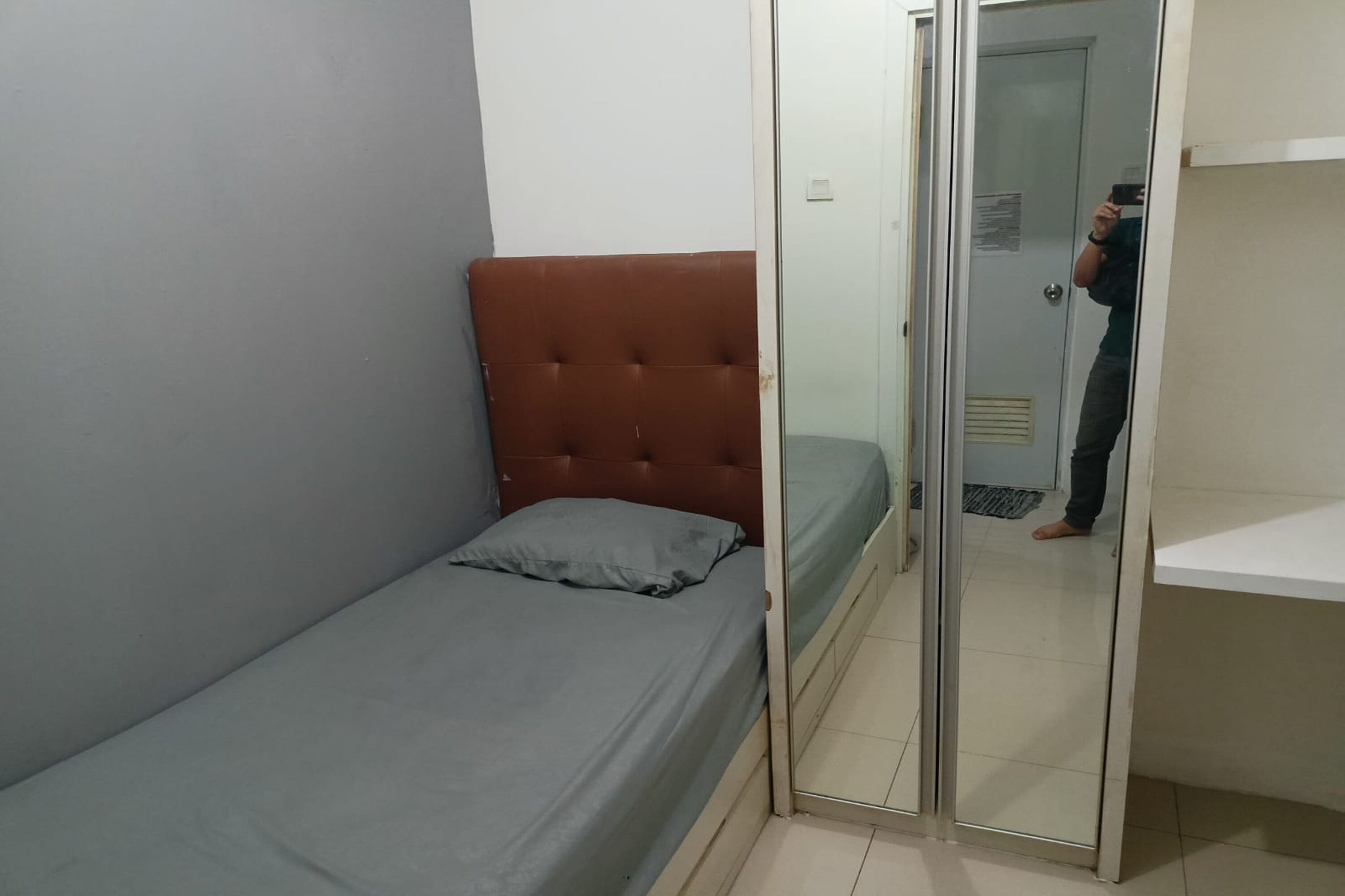 A small, single-bed room with a grey mattress and a brown headboard.