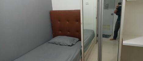 A small, single-bed room with a grey mattress and a brown headboard.