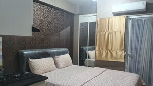 A bedroom with a bed, a bedside table, a mirror, a wardrobe, and an air conditioning unit. - S&A Property 5 (Jakarta)