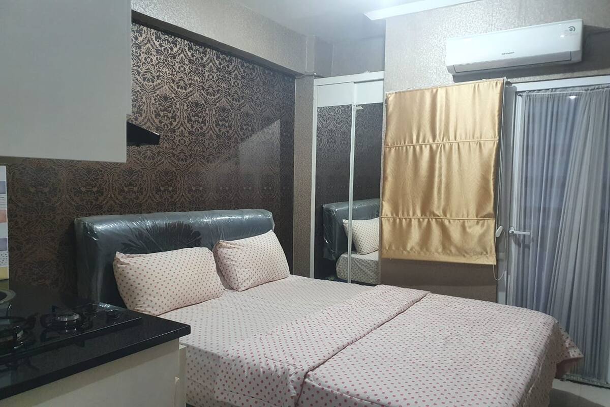A bedroom with a bed, a bedside table, a mirror, a wardrobe, and an air conditioning unit.