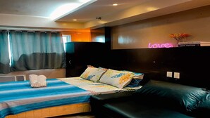 Une chambre d’hôtel moderne avec un lit, un canapé, un néon en forme de cœur et une étagère murale remplie de livres.