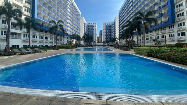Une piscine entourée de grands immeubles dotés de balcons, de palmiers et surplombant un ciel dégagé.