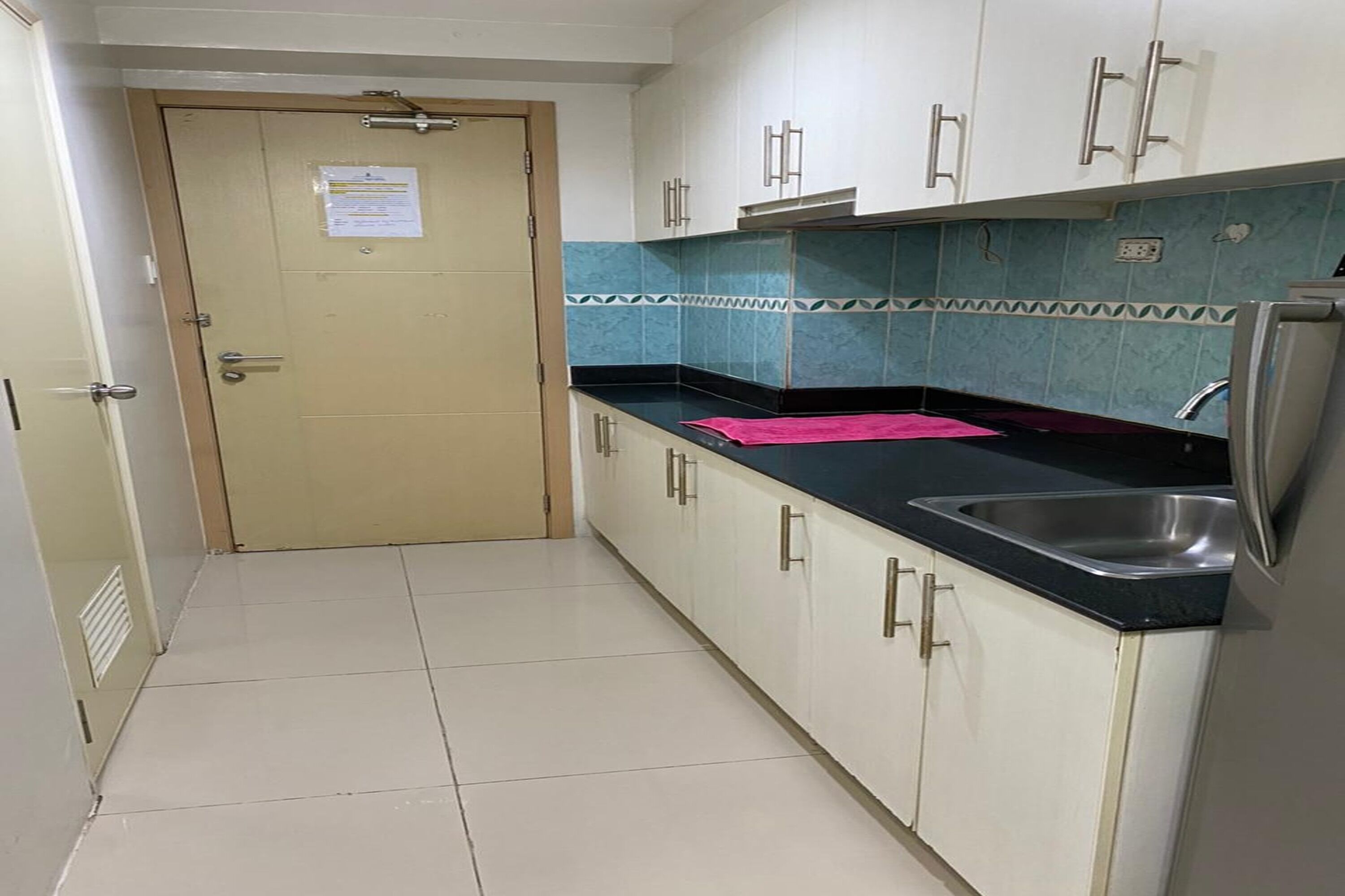 Cocina con armarios blancos, encimera negra, pileta de acero inoxidable y una puerta con un aviso.