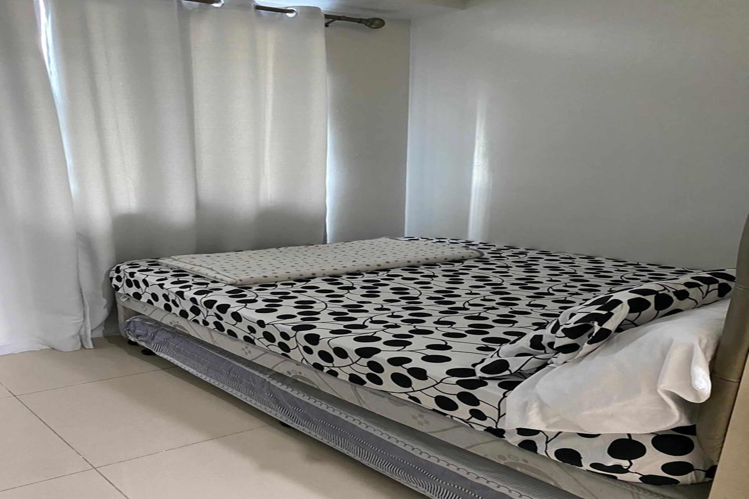Un letto con una coperta a pois bianchi e neri, tende bianche e una testiera bianca.