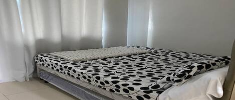 Un lit avec une couvre-lit à pois noirs et blancs, des rideaux blancs et une tête de lit blanche.
