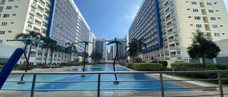 A modern hotel with a central pool, surrounded by high-rise buildings and palm trees.