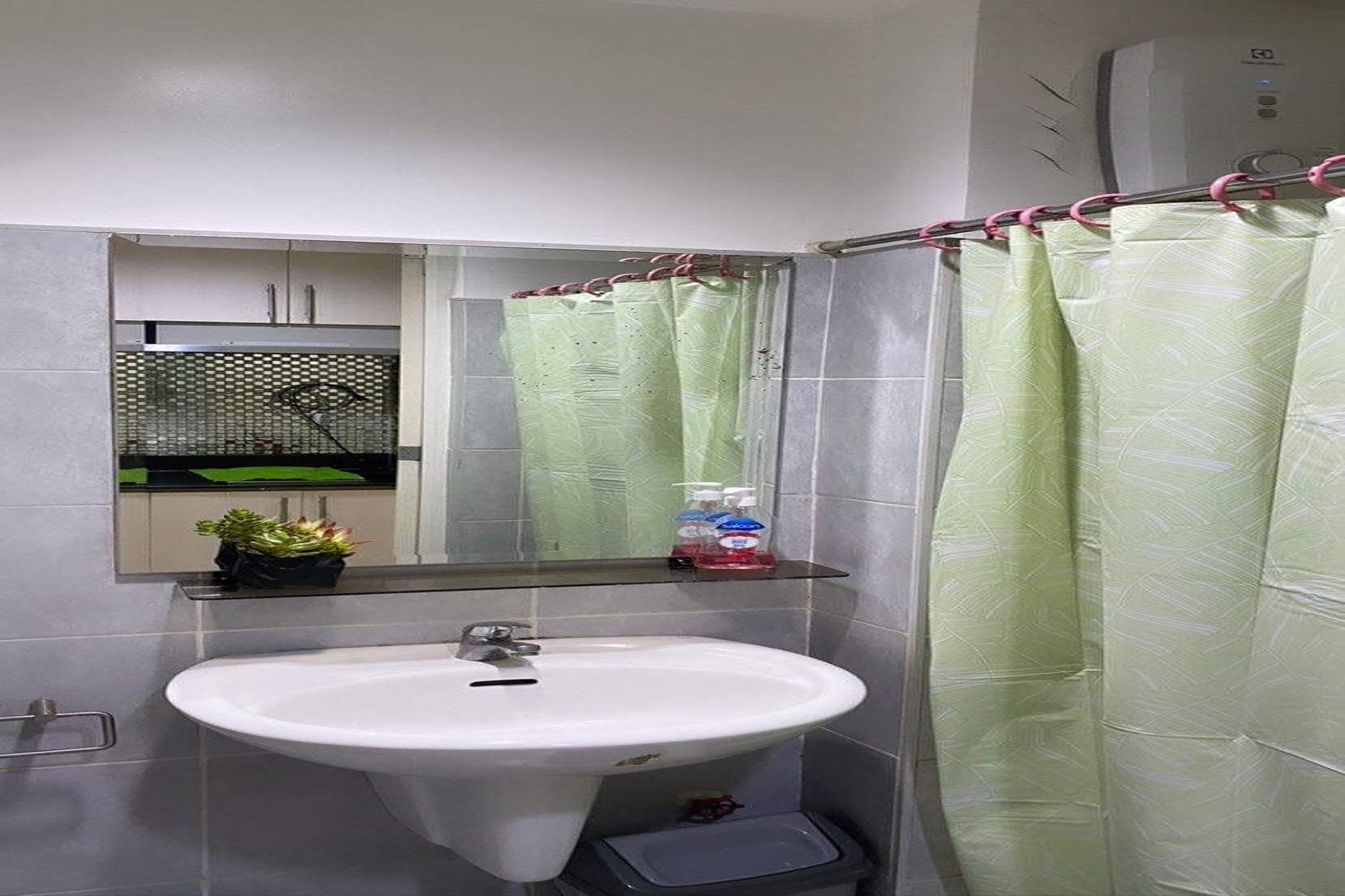 Un baño con un lavabo blanco, un espejo, una cortina de ducha verde y un estante pequeño con artículos de aseo.