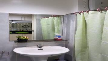 Un baño con un lavabo blanco, un espejo, una cortina de ducha verde y un estante pequeño con artículos de aseo.