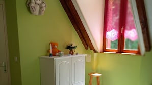 A room with a sloped ceiling, a white wardrobe, a wooden stool, a quilt on the floor, and a window with a red curtain.