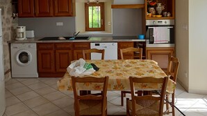 A compact kitchen with wooden cabinets, a washing machine, a dining table with chairs, and a clock on the wall.