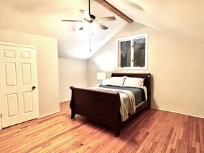A bedroom with a wooden bed, a ceiling fan, a window, and a door.