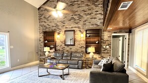A living room with a brick wall, leather sofas, a coffee table, and a ceiling fan.