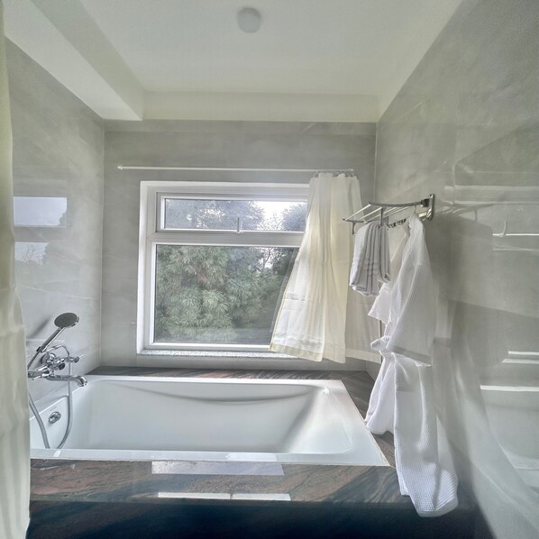 Une salle de bain moderne avec une baignoire sur pieds, une fenêtre donnant sur la verdure et un porte-serviettes avec des serviettes.