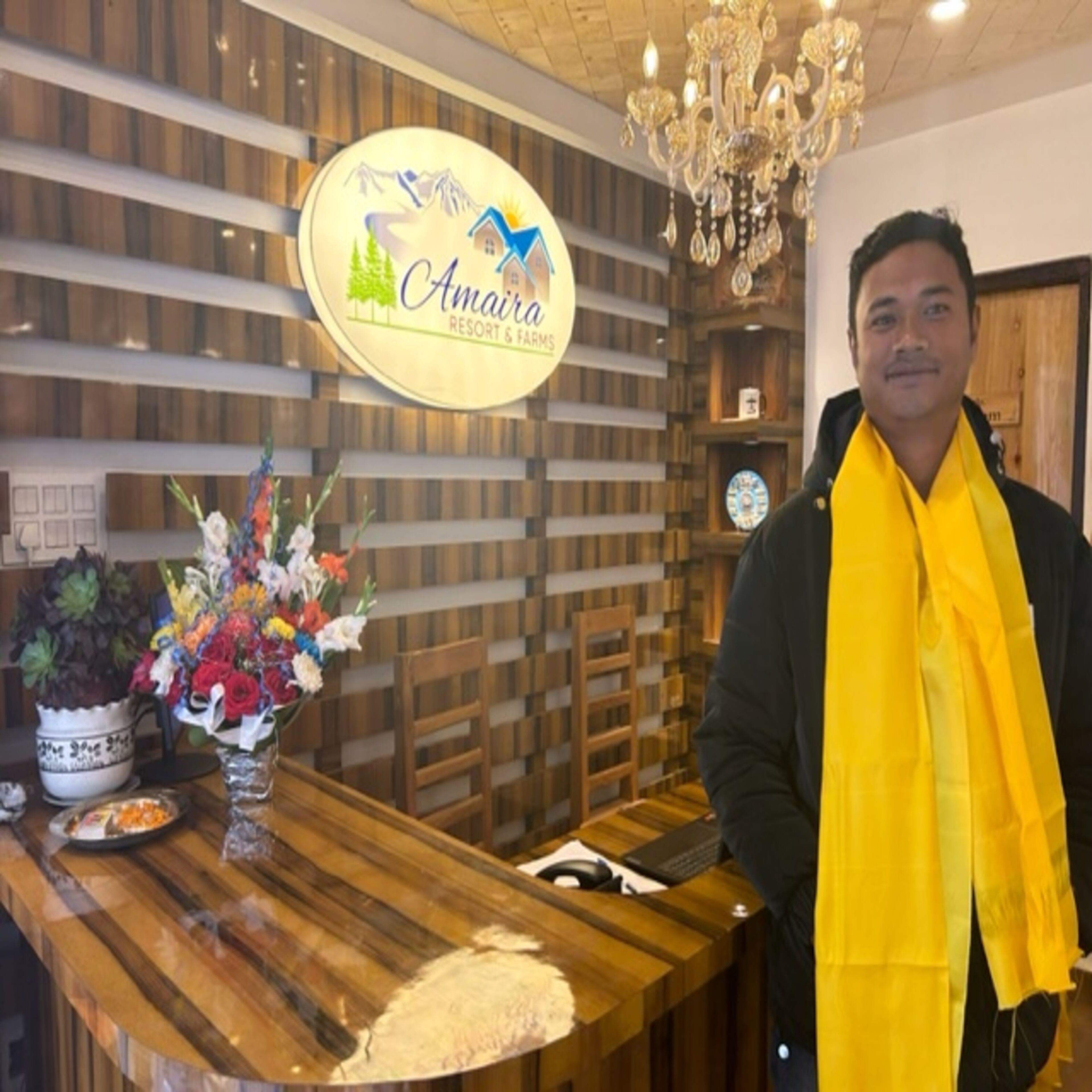 A reception desk at Amaira Resort & Farms with a wooden design, a chandelier, and a sign above the desk.