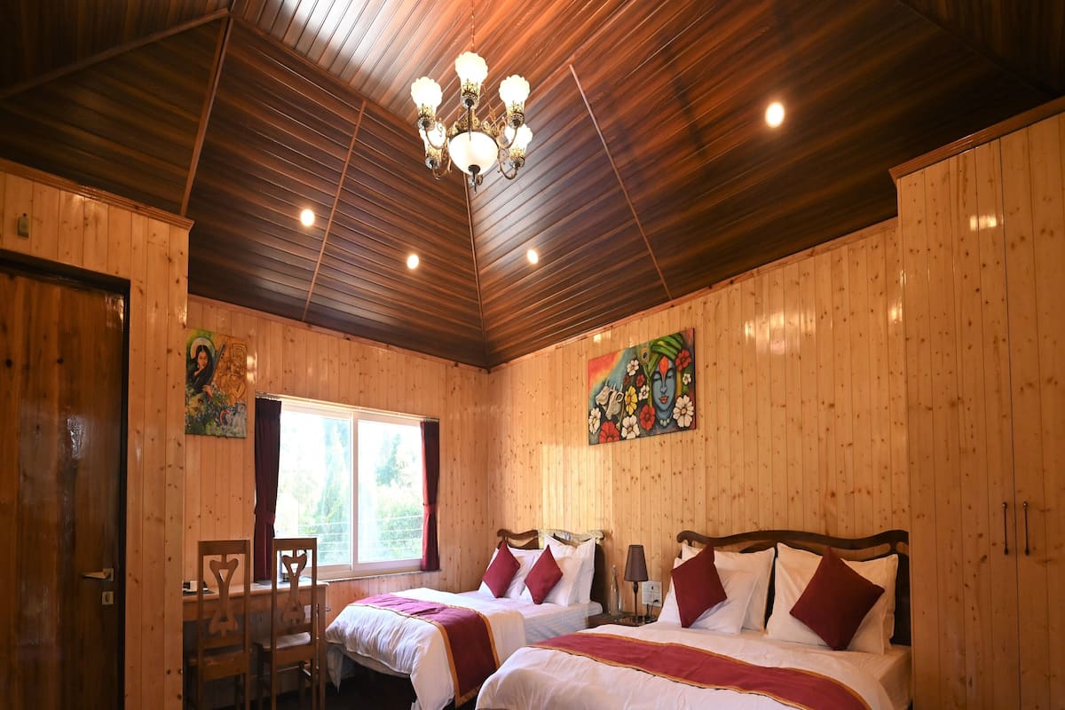 A room with two beds, wooden walls, a chandelier, a window, and a rug.