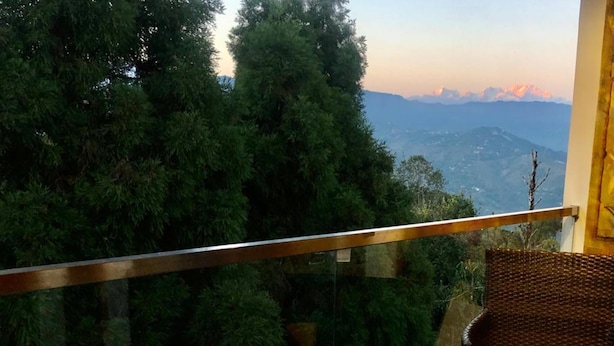 Un balcon doté de meubles en osier, d’une table en verre et offrant une vue sur les montagnes.