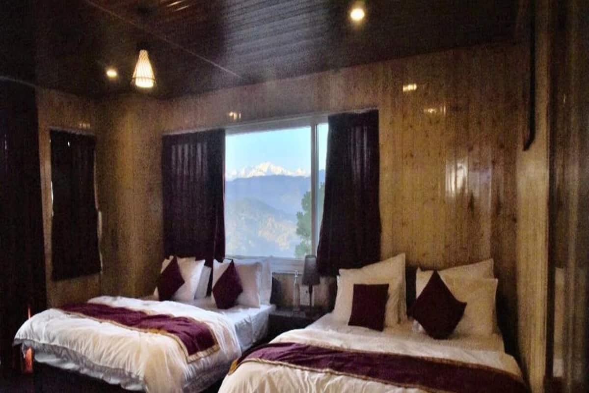 A room with two beds, wooden walls, a large window with a mountain view, and a patterned rug.