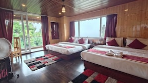 Une chambre d’hôtel avec deux lits, de grandes fenêtres, un ventilateur et une vue sur la verdure.