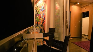 Un balcon doté d’une balustrade en verre, d’une chaise et d’un tableau abstrait aux couleurs vives accroché au mur.