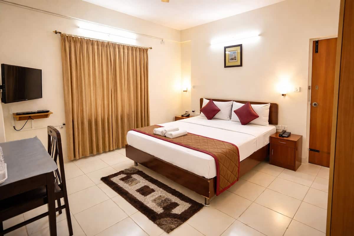 A hotel room with a bed, bedside table, TV, and a desk with a chair.