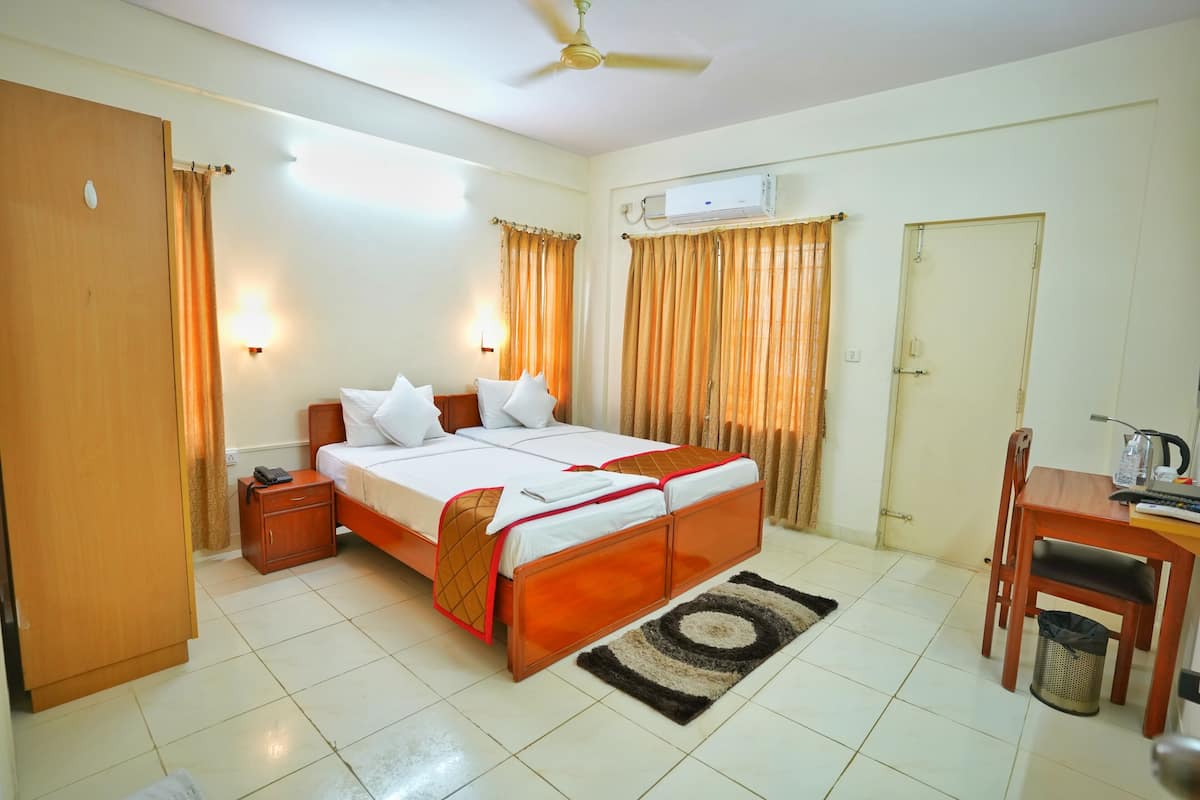 A hotel room with a bed, bedside table, desk, chair, and an air conditioning unit.