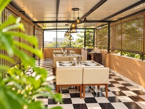 An outdoor dining area with checkered flooring, tables set with plates and cutlery, and hanging pendant lights. - The Altruist Bellandur ORR Hotel (Bengaluru)